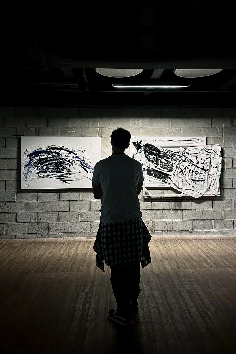Visitor observing abstract unconscious paintings by Juca Máximo in a raw exhibition space — emotional art installation blending texture, gesture and introspection.