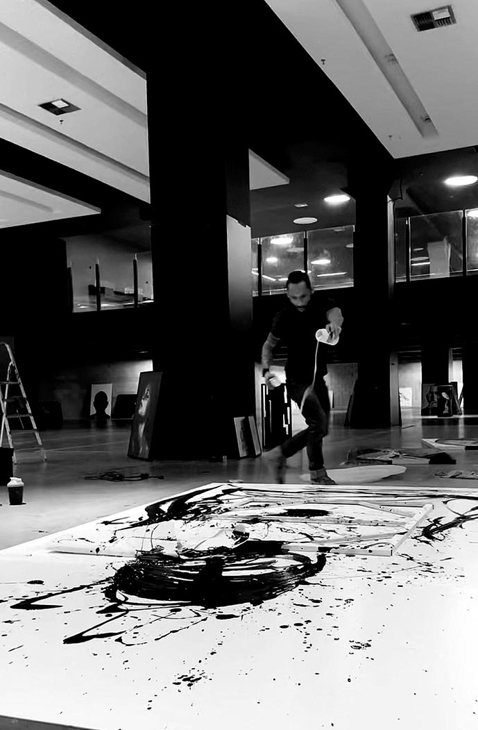 Juca Máximo creating a large-scale emotional painting with instinctive gestures in black and white inside a monumental art space.