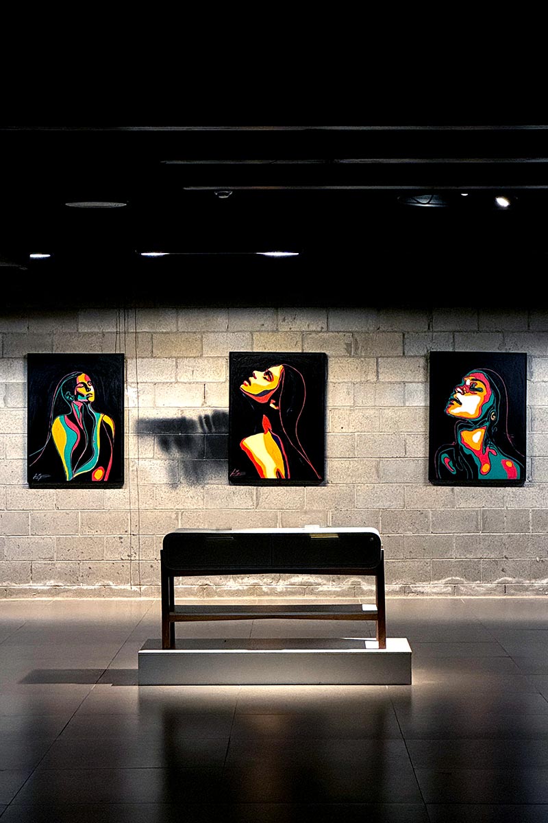 Three vibrant portraits from the Intense series by Juca Máximo displayed in a solo gallery exhibition, capturing emotional intensity through expressive female figures.