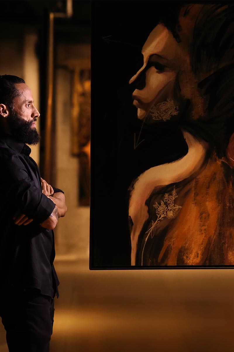 Brazilian artist Juca Máximo observing his emotional expressionist portrait in warm golden tones — contemplative gallery view.