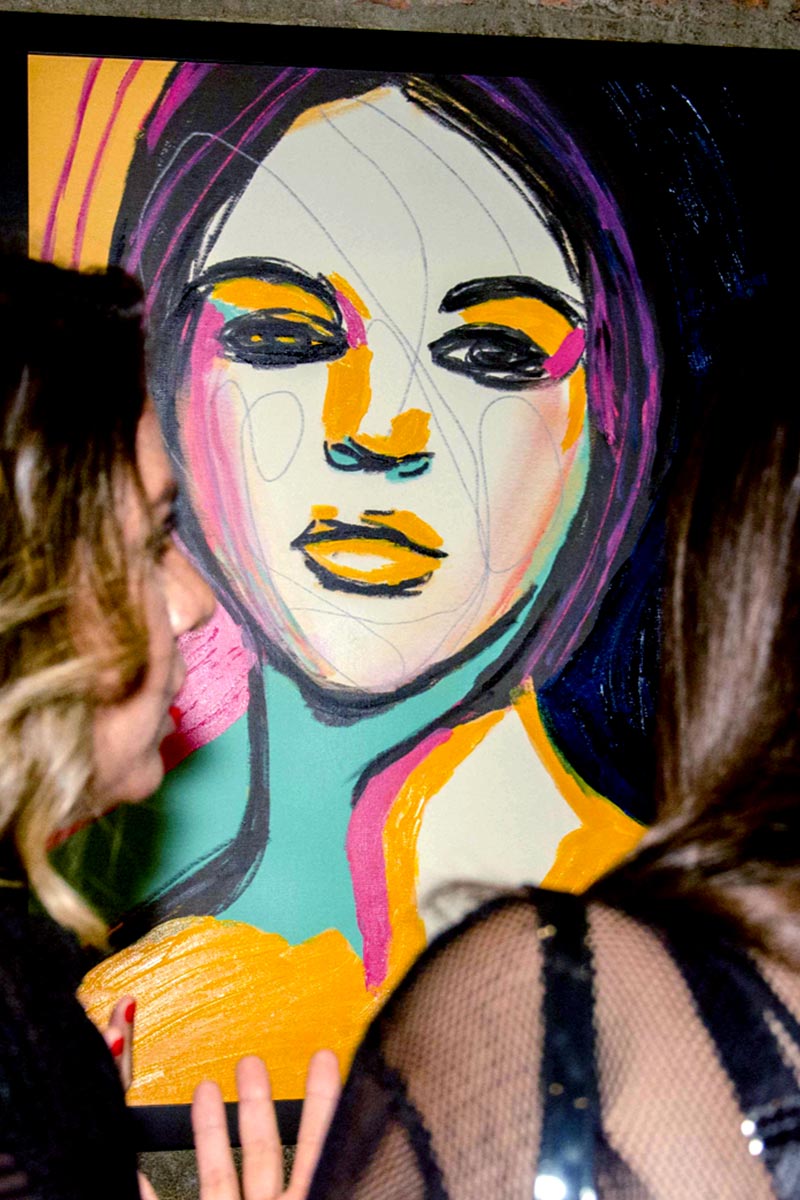 Visitors engaging with a colorful female portrait from the Retails series by Juca Máximo, exhibited in a public contemporary art show.