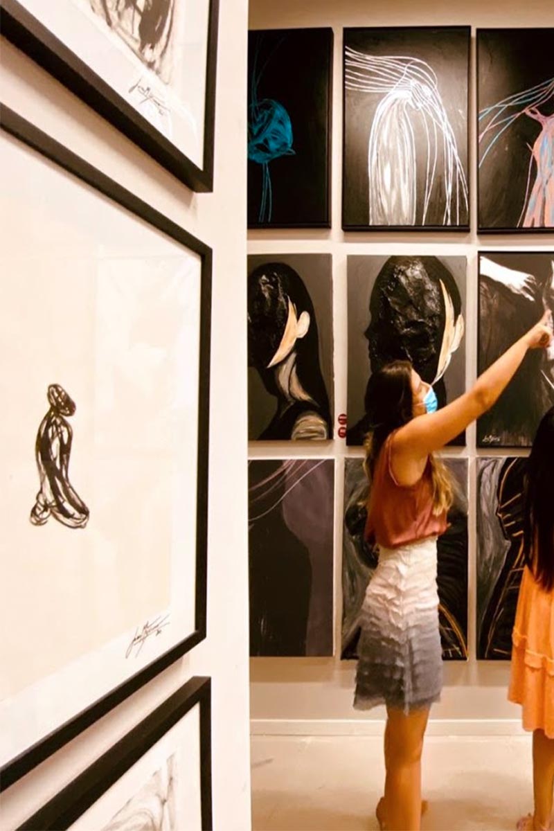 Visitors exploring Juca Máximo's expressive large-scale black paintings and framed emotional drawings during a contemporary art exhibition.