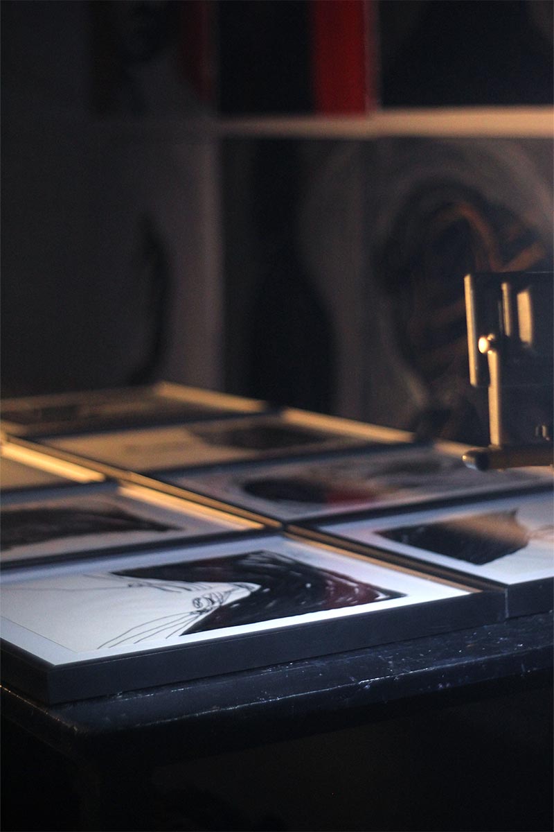 Close-up view of framed emotional black ink drawings by Juca Máximo on a dark studio table with soft lighting and artistic depth.