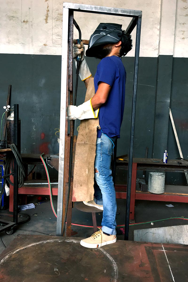 Moment of active welding with sparks flying as the artist builds a tall iron sculpture frame.