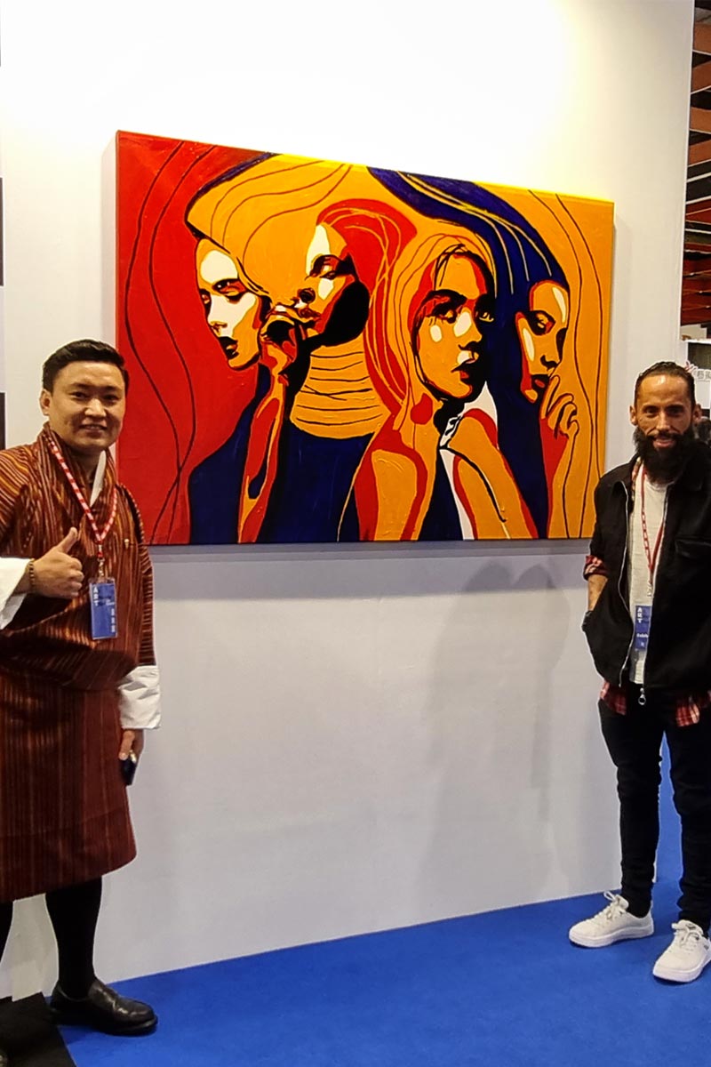 Artist Juca Máximo standing next to a collector in front of one of the main paintings from the 'Write Your Story' series during an international show.