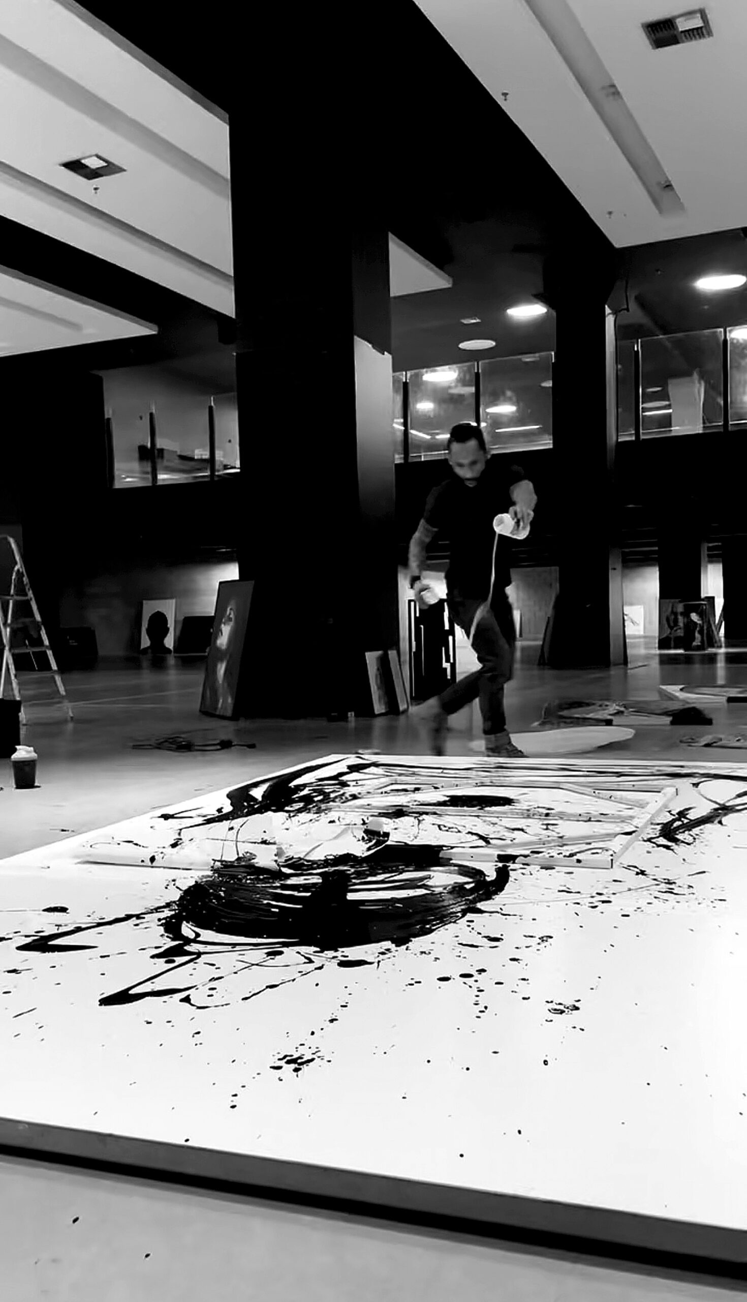 Brazilian contemporary artist Juca Máximo creating an expressive abstract painting using full-body gestures in his art studio. Black acrylic paint spreads across a large white canvas, evoking intensity and movement. The scene captures the emotional process behind the artwork, blending physical performance and conceptual depth.