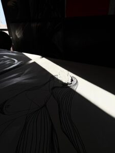 Traces artwork by Brazilian contemporary artist Juca Maximo — minimalist black line art figure on white canvas, illuminated by a diagonal beam of natural light in the artist’s studio, highlighting textures, shadows, and poetic details. Contemporary figurative art with abstract expressionist gestures, collectible original painting.