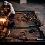 Artist welding an iron installation in the studio, sparks flying as metal fragments and tools surround the worktable during the construction process of the Absence installation.