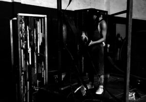 Artista soldando escultura em ferro no estúdio, utilizando máquina de solda em estrutura metálica da série Energy, explorando tensão, fogo e construção física da obra em processo. Artist welding an iron sculpture in the studio, using a welding machine on a metal structure from the Energy series, exploring tension, fire, and the physical construction of the artwork in process.