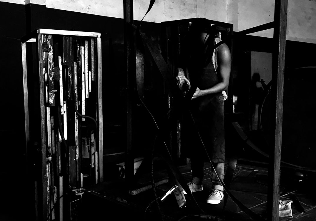 Artista soldando escultura em ferro no estúdio, utilizando máquina de solda em estrutura metálica da série Energy, explorando tensão, fogo e construção física da obra em processo. Artist welding an iron sculpture in the studio, using a welding machine on a metal structure from the Energy series, exploring tension, fire, and the physical construction of the artwork in process.